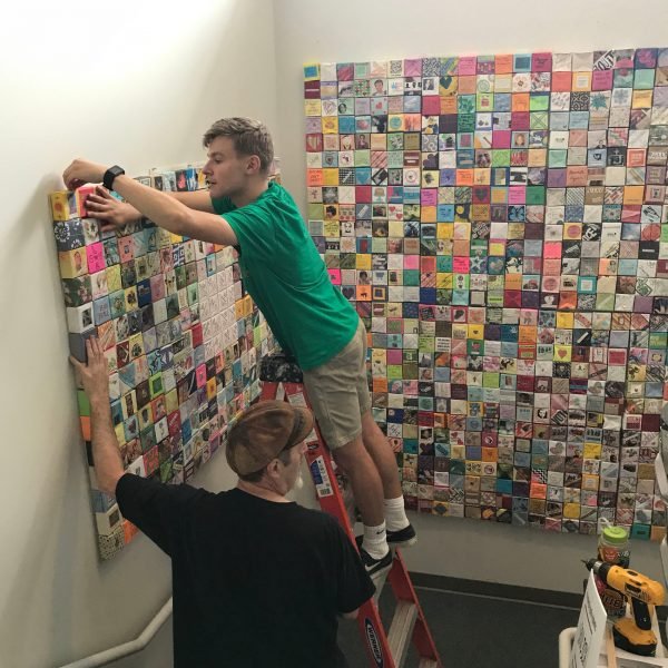 Two men with ladder install display panels in stairway